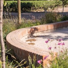 a circular brick bench in the middle of a garden with wildflowers growing around it