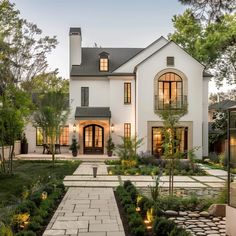 a large white house with lots of windows and plants in the front yard at dusk