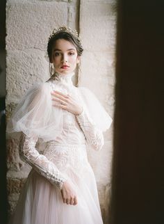 a woman in a white dress standing next to a stone wall wearing a tiara