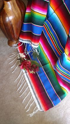 a colorful blanket sitting on the floor next to a wooden vase with flowers in it