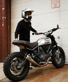 a man standing next to a motorcycle in front of a garage door with a helmet on