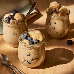 three jars filled with oatmeal and blueberries on top of a wooden table