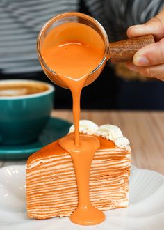 someone pouring orange juice onto a piece of cake on a plate with a cup of coffee in the background