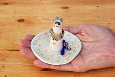 a person holding a small white plate with a tiny cat on it's top