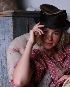 a woman sitting in a chair with a hat on her head and one hand near her face