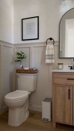 a white toilet sitting in a bathroom next to a wooden cabinet and sink with a mirror above it