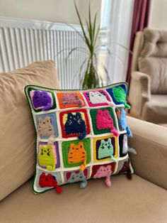 a crocheted pillow with cats on it sitting on a couch next to a potted plant