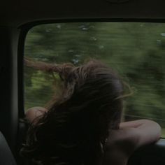 a woman sitting in the back seat of a car with her hair blowing in the wind