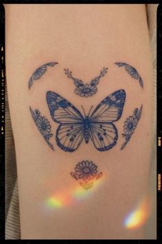 a blue butterfly tattoo on the back of a woman's left thigh, with flowers and butterflies around it