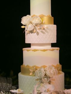 three tiered wedding cake with white flowers and gold trimmings on the top