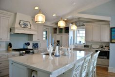 a kitchen with white cabinets and an island in the middle is lit by three pendant lights