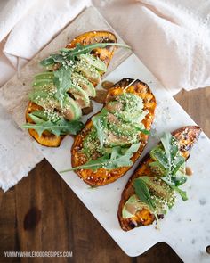 four grilled sweet potatoes topped with avocado and sprouts on a cutting board