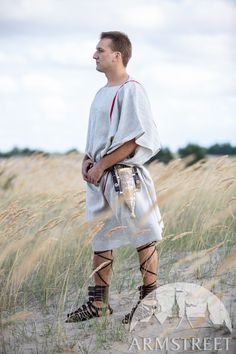 a man in roman garb standing on the sand with his hands behind his back