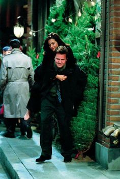 a man and woman are walking down the street in front of a christmas tree display