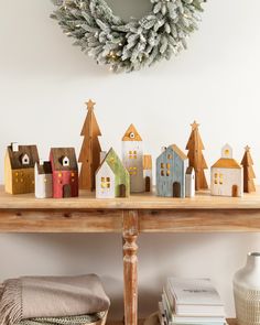 a table topped with small wooden houses next to a christmas wreath on top of a wall