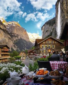 a table with food on it in front of a mountain range and waterfall, surrounded by mountains