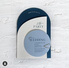 a blue and white wedding card with a ring on it's side, sitting against a wall