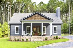 a small blue house in the woods with porches and chairs on the front lawn