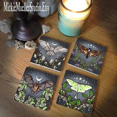 four square coasters with bats and flowers on them next to a candle, some rocks and a glass jar