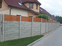 a house that is next to a fence with grass in front of it and cars parked on the side of the road