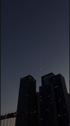 the sun is setting behind two tall buildings in front of an airplane flying over them