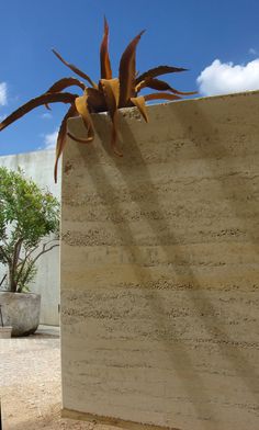 a sculpture in the shape of a spider on top of a block of concrete with a plant growing out of it