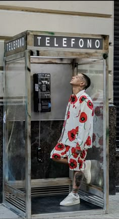 a man standing in front of a phone booth with his face up to the sky