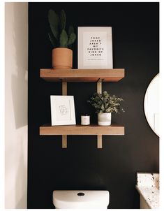 a bathroom with black walls and wooden shelves on the wall, white toilet and potted plants