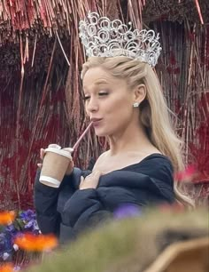 a woman wearing a tiara and drinking from a cup with a straw in her mouth