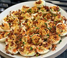 deviled eggs with bacon and chives on a white platter, ready to be eaten