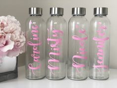 three clear water bottles with pink lettering on them and a flower in the vase next to it