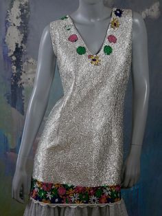 This stunning space age sleeveless flapper dress has a V neckline in the front and back, with the front neckline decorated with yellow, pink, green, and blue embroidered flowers. The silver soft foil dress has a fitted waistline, and the foil part of the dress ends below the hip line with a 4.5-inch (11.43cm) band of embroidered flowers, which then gives way to a two-layer sheer silver ruffle to below the knee. The foil fabric of this dress is durable but soft, and the dress is expertly crafted Retro Sleeveless Spring Party Dress, Retro Sleeveless Dress For Spring Party, Foil Dress, Mad Men Dresses, Formal Cocktail Party, European Vintage, Plaid Blazer, Silver Dress, Space Age