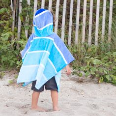 a little boy wearing a blue and white towel on top of a sandy beach next to a fence