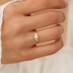 a woman's hand wearing a gold ring with a pearl and diamond accent on it