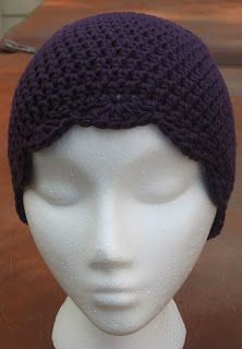 a white mannequin head wearing a purple crochet hat on top of a table