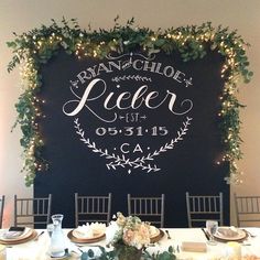 a table set up for a wedding reception with flowers and greenery on the wall