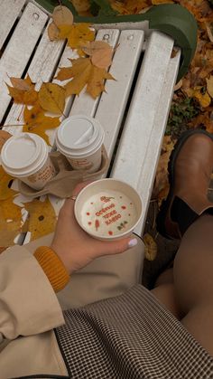 a person sitting on a white bench holding a bowl of food and two coffee cups