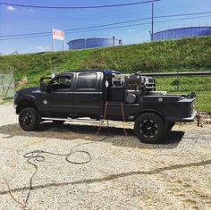 a black truck parked on top of a gravel road next to a green hillside and power lines