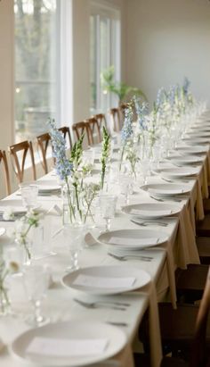 a long table is set with white plates and flowers in vases on each side