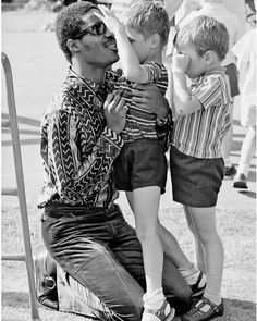 a black and white photo of a man holding two young boys on his lap, with other people in the background