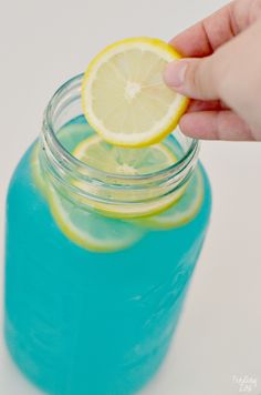 a hand holding a lemon over a jar filled with blue liquid