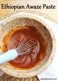 a bowl filled with sauce and whisk on top of a woven table cloth