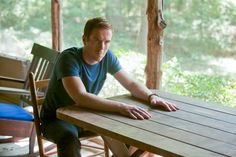 a man sitting at a wooden table with his hands on the table and looking off into the distance