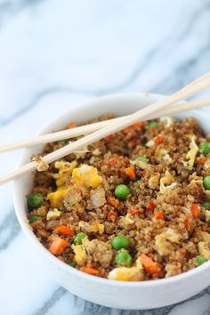 rice with peas and carrots in a white bowl next to wooden chopsticks