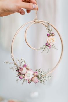 a person holding a hoop with flowers hanging from it's side and another hand reaching for the flower