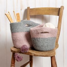 two knitted baskets sitting on top of a wooden chair next to knitting needles and yarn