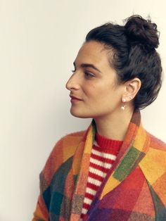 a woman wearing a multicolored jacket and striped sweater looks off to the side