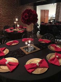 a black table with red napkins and gold plates on it is set for an event