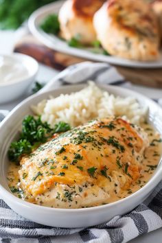 a white bowl filled with chicken and gravy next to rice on a table