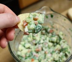 a hand holding a tortilla chip with cucumber salad in it